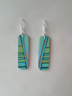 two wooden earrings with blue and green designs on them, hanging from silver ear wires