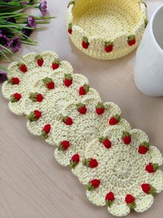 crocheted coasters with red roses on them next to a cup and flower pot holder