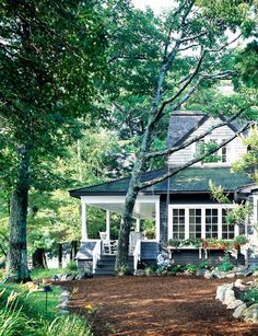 a house in the woods surrounded by trees and shrubs, with white trim on the roof