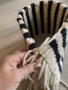 a hand holding a black and white striped crochet basket with tassels