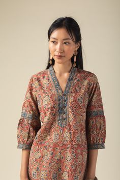 This rust-colored cotton kurta features a vibrant multi-color Kalamkari print, adding an artistic flair. The yoke is elegantly highlighted with a border, sequins, mirror work, buttons, and intricate thread detailing. It has a stylish V-neck collar, 3/4th sleeves adorned with a border and crochet lace, and a convenient side pocket. The straight fit design ensures both comfort and a flattering silhouette.. Pair it with our cotton pant for a cohesive look that exudes confidence. Kurti Collar Neck Design, V Neck Collar Kurta, Straight Kurti Designs Cotton, Kalamkari Dresses Kurti, Kurta Sleeves Design, Kalamkari Kurti Designs, Kalamkari Kurta Designs, Kurta With Collar, V Neck Kurti Design