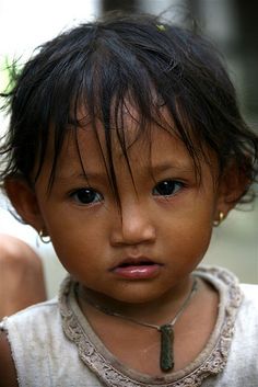 a close up of a young child wearing a necklace and looking at the camera with a serious look on his face