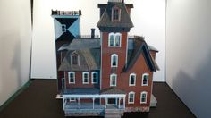 a paper model of a house on display in a room with white walls and brown flooring