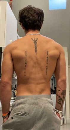 the back of a man with tattoos on his upper and lower half, standing in a kitchen