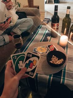 two people sitting on a couch holding cards and wine bottles in front of the table