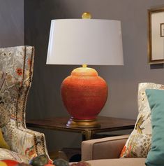 an orange vase sitting on top of a table next to a chair with a lamp