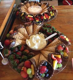 two platters filled with ice cream, fruit and chocolate covered waffle cones on top of a wooden table