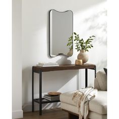 a mirror sitting on top of a wooden table next to a white couch and potted plant