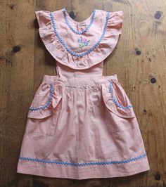 a pink dress with blue trims on the chest and collar, sitting on a wooden floor