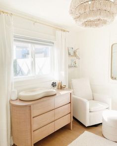 a living room with white furniture and a chandelier hanging from the ceiling above it