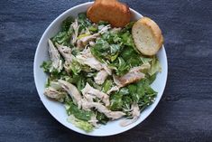 a white bowl filled with lettuce and chicken next to two slices of bread