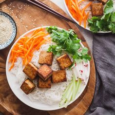 two plates filled with tofu, carrots and rice on top of a wooden cutting board