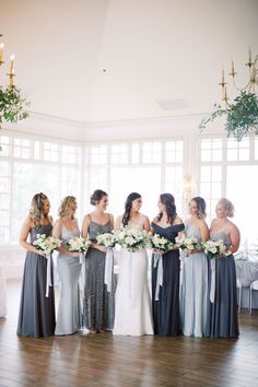 a group of women standing next to each other in front of a window holding bouquets