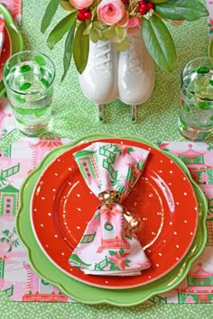 the table is set with red and green plates, napkins, and flowers in vases