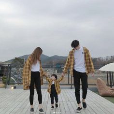 a man and woman holding hands while walking with a small child on a wooden deck