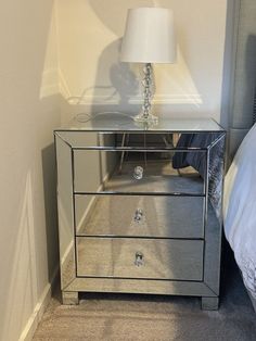 a mirrored night stand with a lamp on top and a bed in the corner behind it