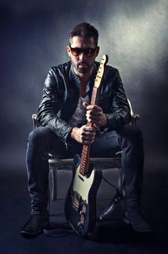 a man sitting on top of a chair holding an electric guitar in front of his face