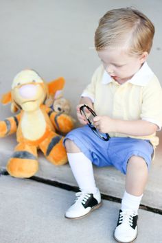 a little boy sitting next to a stuffed animal on the ground and playing with scissors