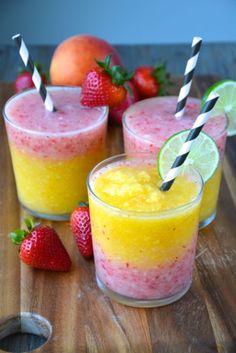 three glasses filled with fruit and drink on top of a wooden table next to some strawberries