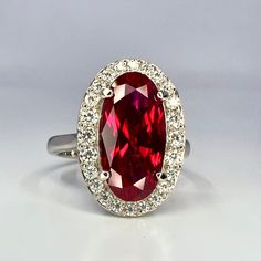 an oval shaped ruby and diamond ring on a white surface with the center stone surrounded by smaller diamonds