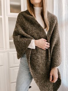 a woman standing in front of a window wearing a brown cardigan sweater and jeans