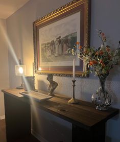 a painting hangs on the wall next to a table with flowers and candles