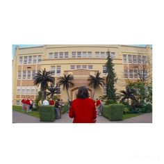 a woman standing in front of a large building with palm trees on the side walk