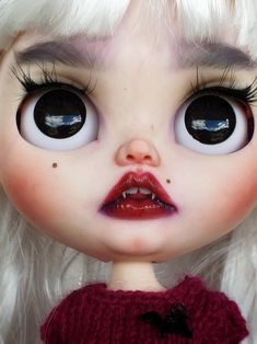 a close up of a doll with big eyes and white hair wearing a red sweater