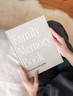 a person sitting on a bed holding a book in front of their face with the title family memory book