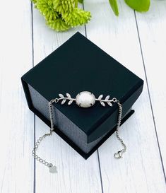 a black box with a silver bracelet on top of it and flowers in the background