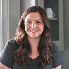 a woman with long brown hair smiles at the camera while standing in front of a window