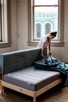 a woman unpacking a mattress in front of a window with a blue sheet on it