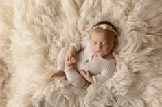 a newborn baby is laying on a fluffy blanket and wearing a white knitted outfit