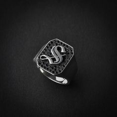 a signet ring with the letter s in silver and black diamonds on a black background