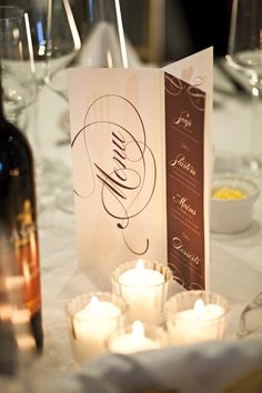 the table is set with wine glasses, candles and an open menu card on it