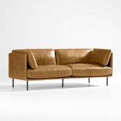 a tan leather couch with two pillows on it's back and one arm extended