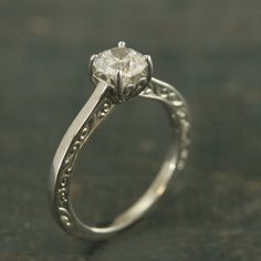 a diamond ring with filigrees on the sides and an engraved band around it