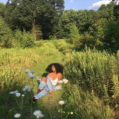 a woman sitting in the middle of a field surrounded by tall grass and wildflowers