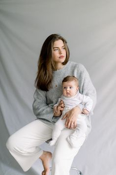 a woman is holding a baby in her lap and posing for a studio photo with white backdrop