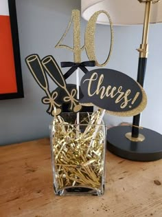 a table topped with a glass vase filled with gold foil and a sign that says cheers