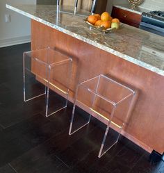 two acrylic stools sitting in front of an island with fruit on it