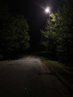 an empty road at night with street lights on the side and trees in the background