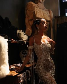 a woman in a silver dress standing next to a table with some jewelry on it