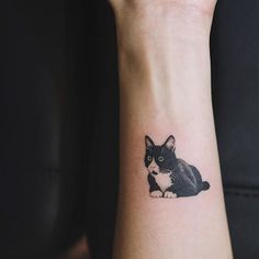 a small black and white cat tattoo on the wrist