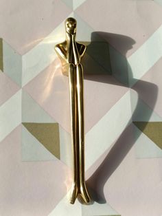 a gold colored brooch with a woman figure on it's back, standing in front of a geometric background