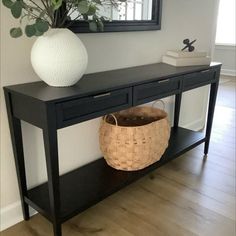 a black console table with a basket underneath it and a mirror on the wall behind it