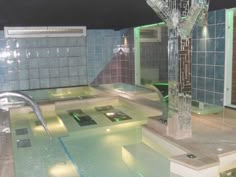 an indoor swimming pool is lit up with green lights and water features on the walls