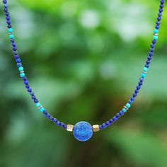 Thailand's Somluck Komolmith demonstrates her eye for fine detail and manual dexterity in this hand-beaded pendant necklace. A polished sphere of lapis lazuli commands your attention complemented by a beaded pattern featuring smaller lapis beads howlite beads and brass beads. On either side of the pendant golden hematite beads provide a visual anchor. The necklace features a spring ring clasp and extender chain of sterling silver. Bohemian Sapphire Round Bead Jewelry, Bohemian Sapphire Beaded Jewelry, Lapis Lazuli Crystal Necklace With Gemstone Beads, Lapis Lazuli Gemstone Beads Crystal Necklace, Adjustable Gemstone Beads Round Pendant Necklace, Adjustable Gemstone Beaded Round Pendant Necklace, Round Beaded Lapis Lazuli Jewelry With Natural Stones, Spiritual Lapis Lazuli Beaded Necklaces, Sapphire Beaded Necklaces With Natural Lapis Lazuli Stones