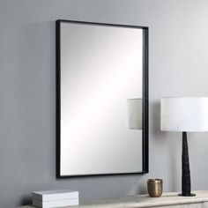 a large mirror on the wall next to a table with a lamp and lampshade