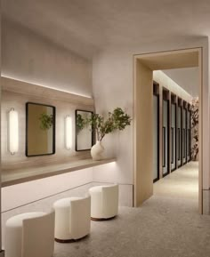 an empty hallway with white stools and mirrors on the wall, along with potted plants